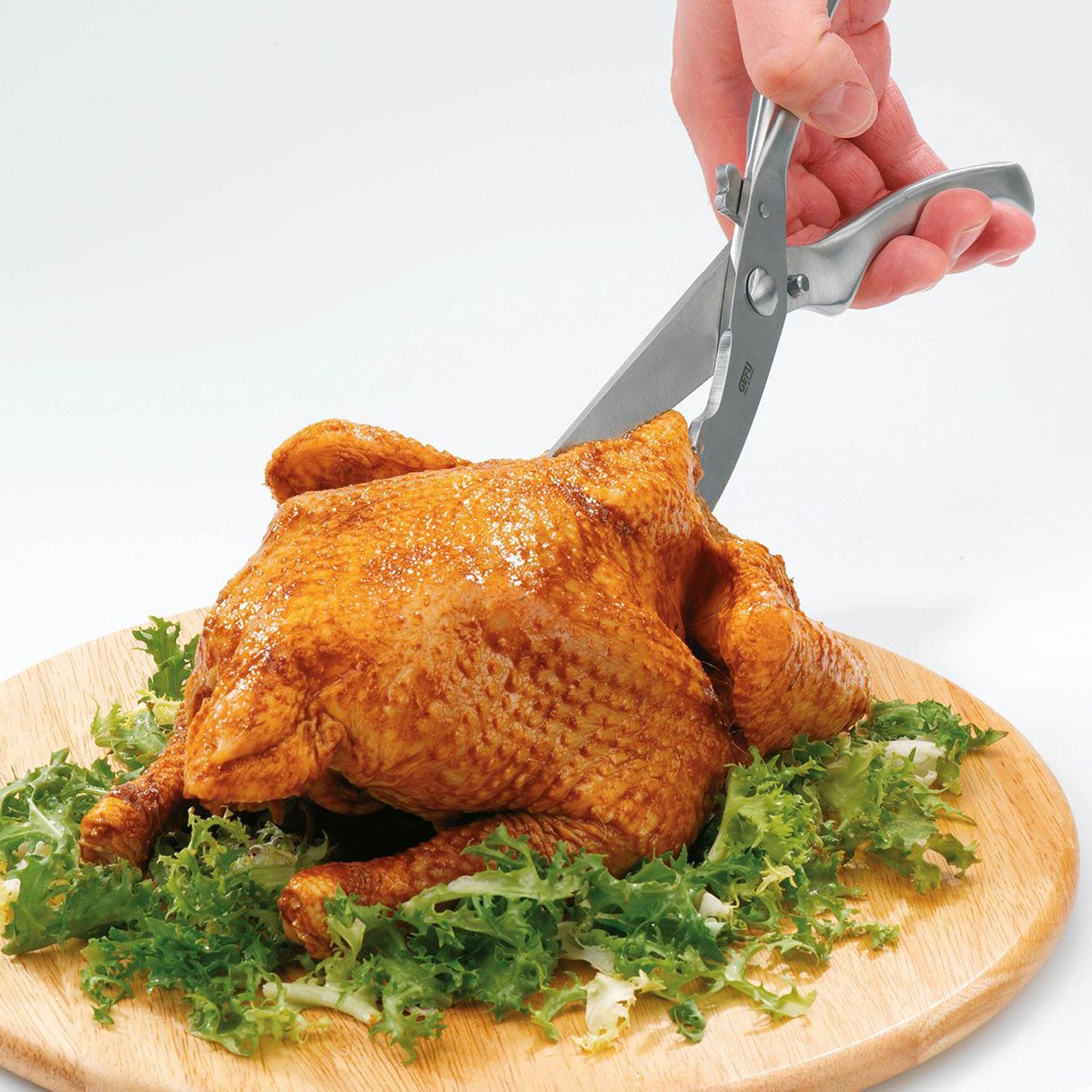 Poultry shears cutting a whole chicken on a wooden board