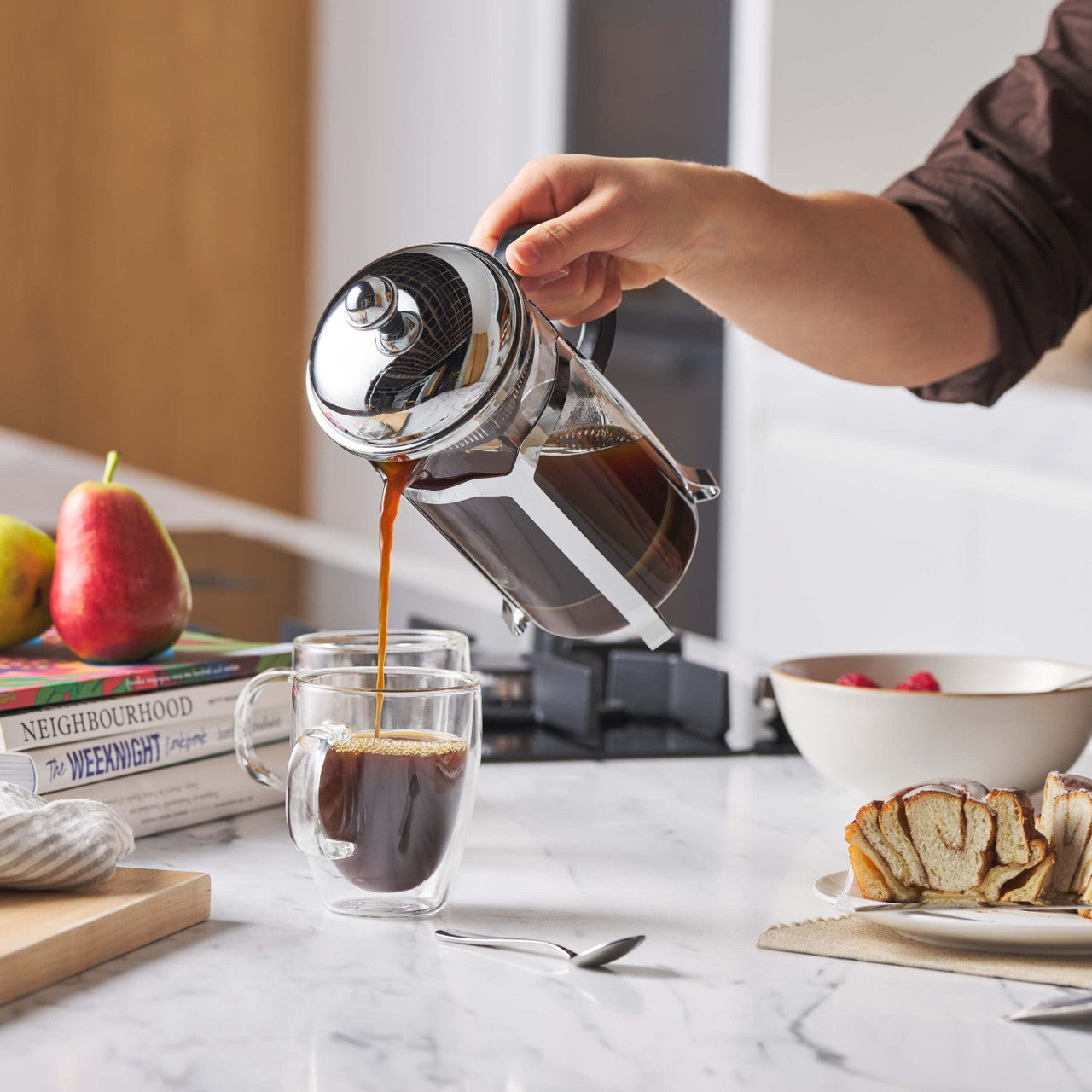 Stainless coffee plunger pouring dark coffee into a clear mug with glass carafe