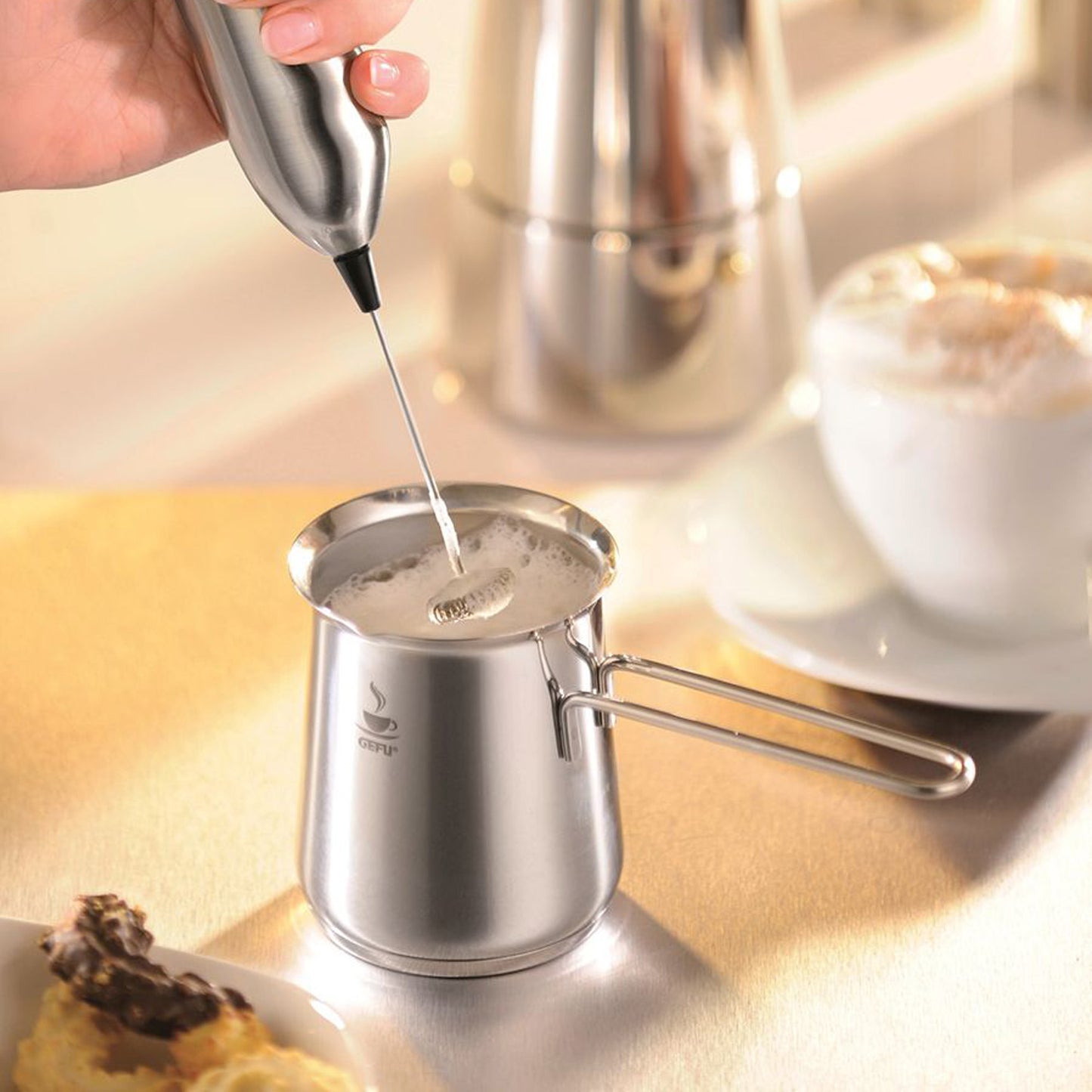 Stainless-steel milk frothing jug with pouring spout, being filled, GEFU logo