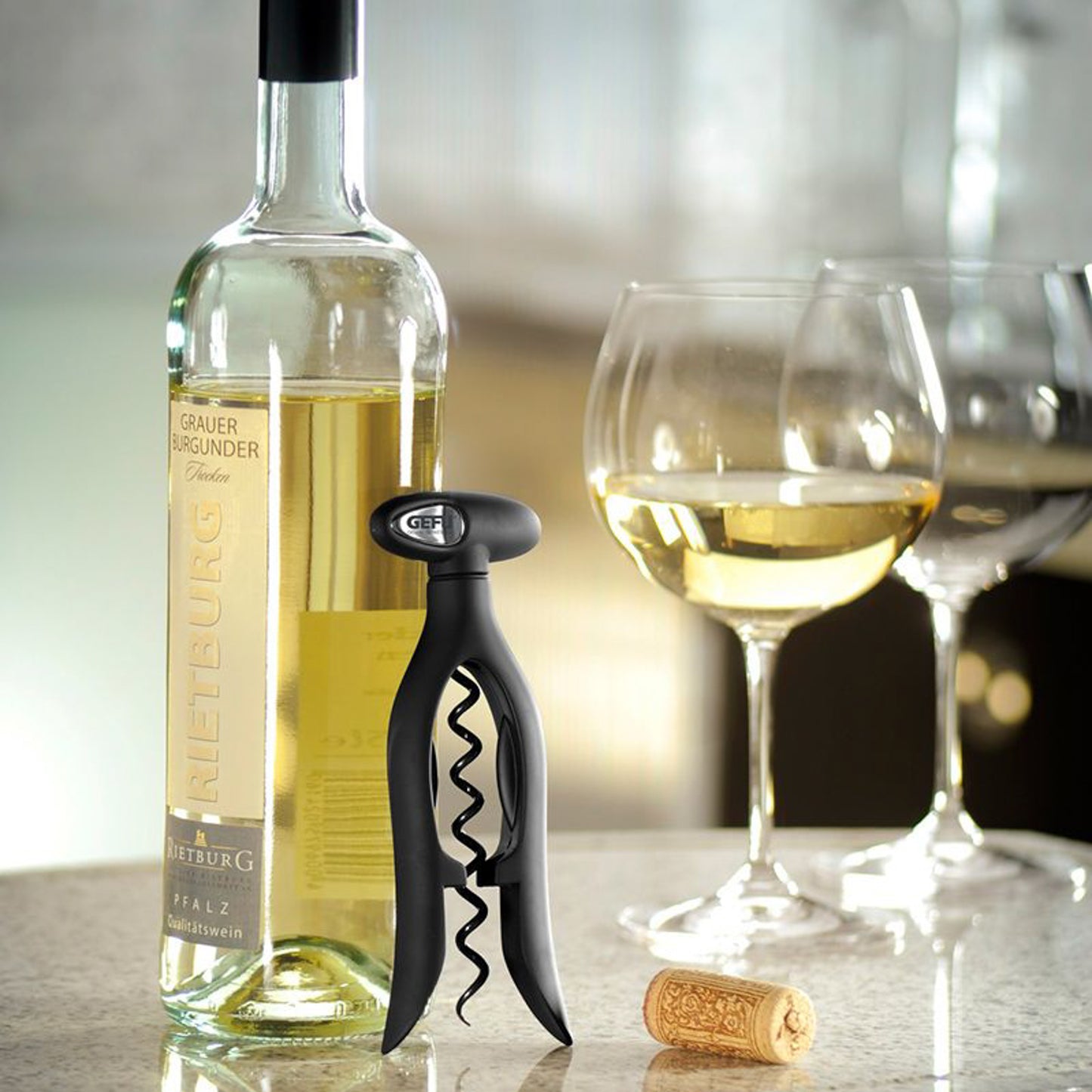 Black corkscrew with spiral worm beside bottle and wine glass, holding a cork