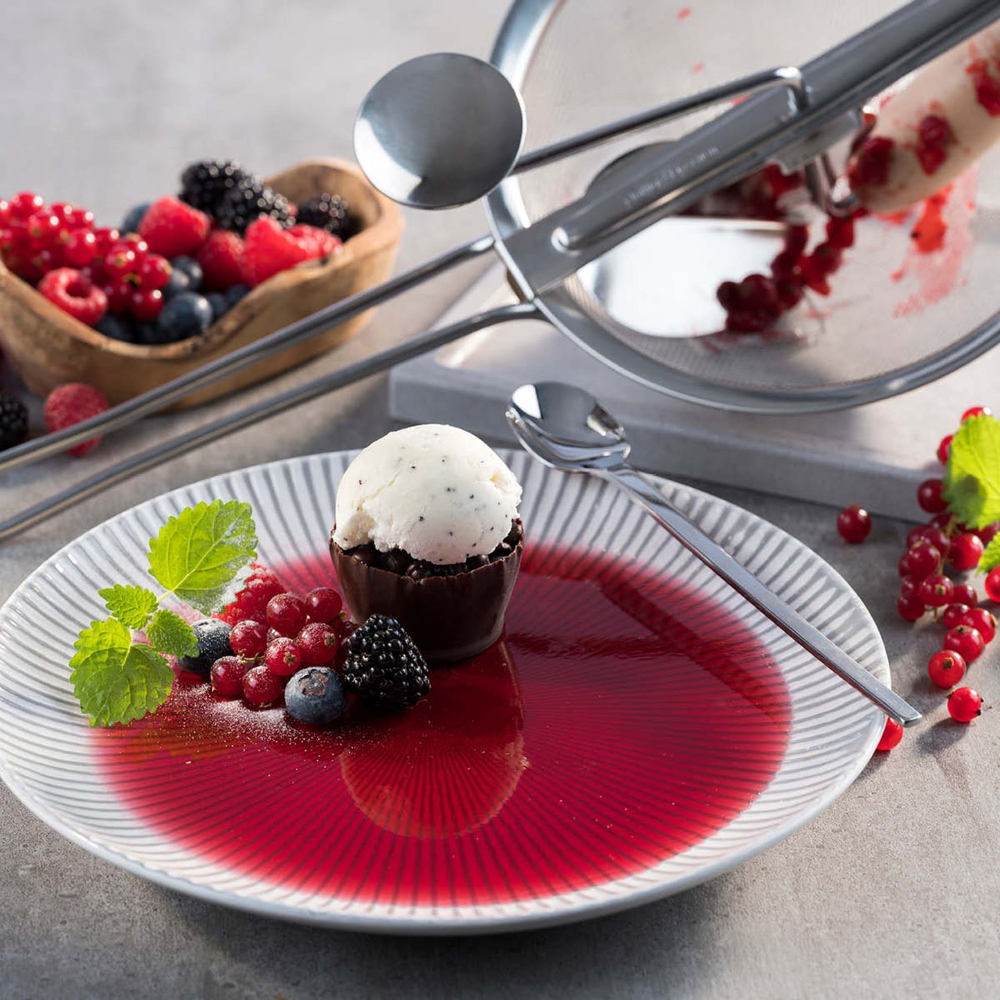 Stainless-steel strainer press attachment with mesh, positioned over a berry-covered plate