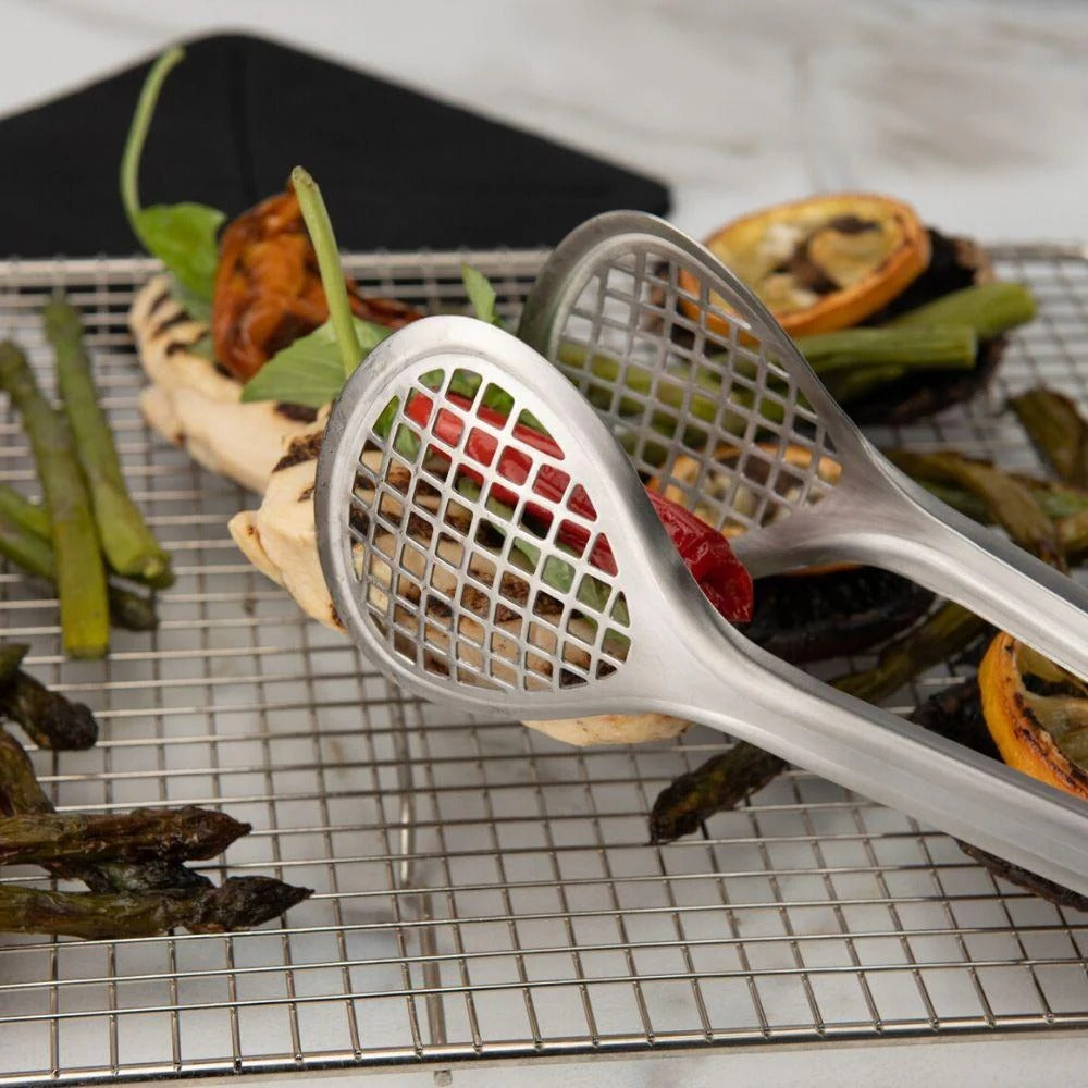 Wide stainless steel grill tongs with mesh scoop lifting food off a wire rack