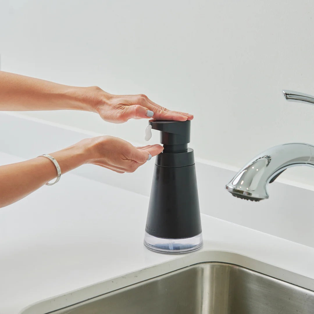 Black foam pump dispenser being pressed by hands over a sink