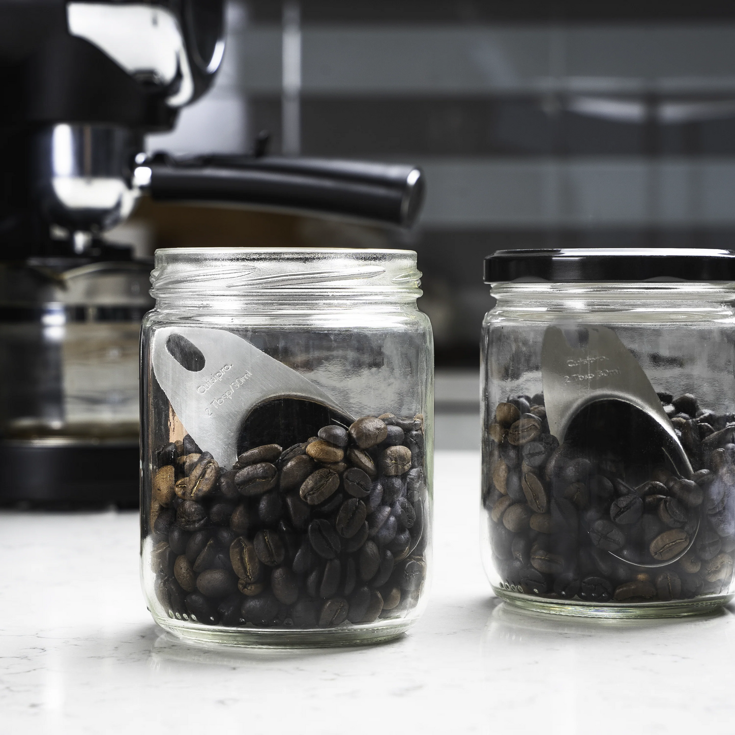 Jar of dark coffee beans with stainless-steel scoop-shaped insert