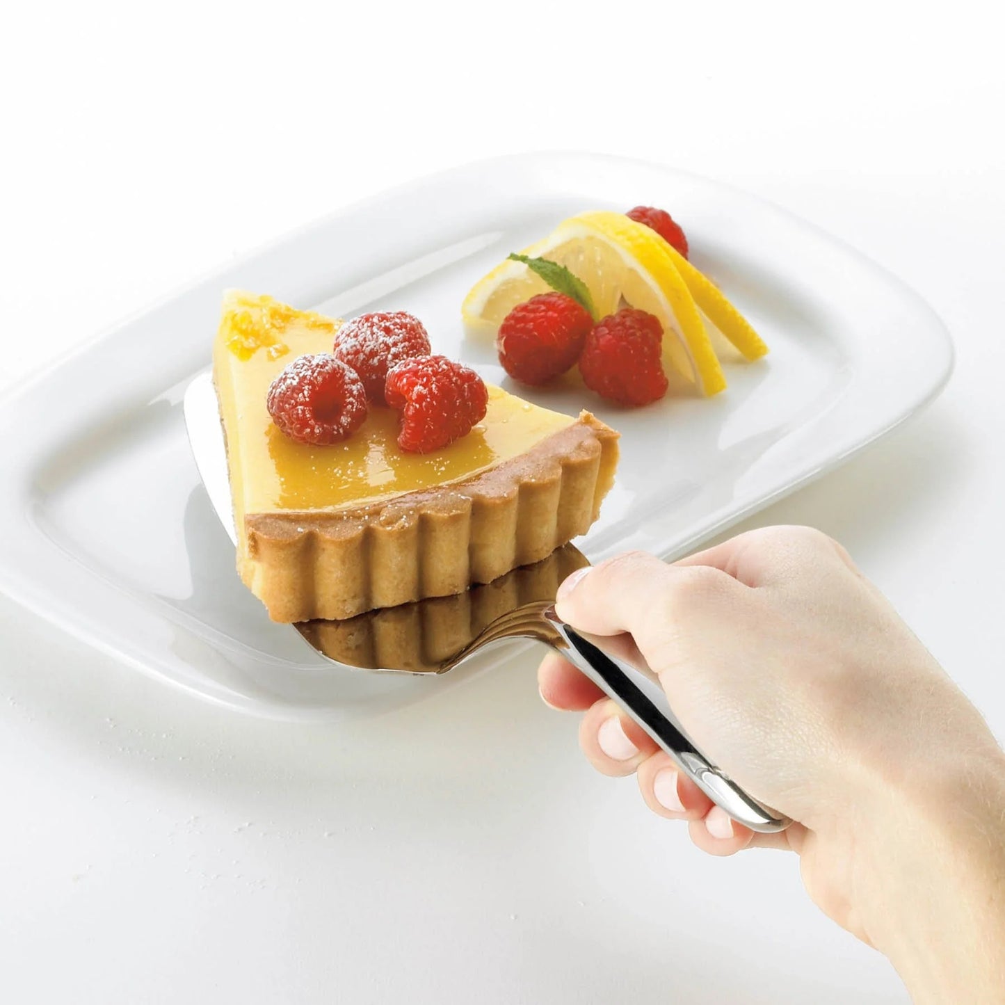 Mini cake/pie server lifting a small tart with berries and lemon garnish