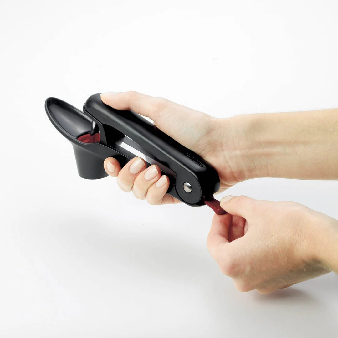 Hand-held pitter tool clamped over a cherry, showing red inner opening