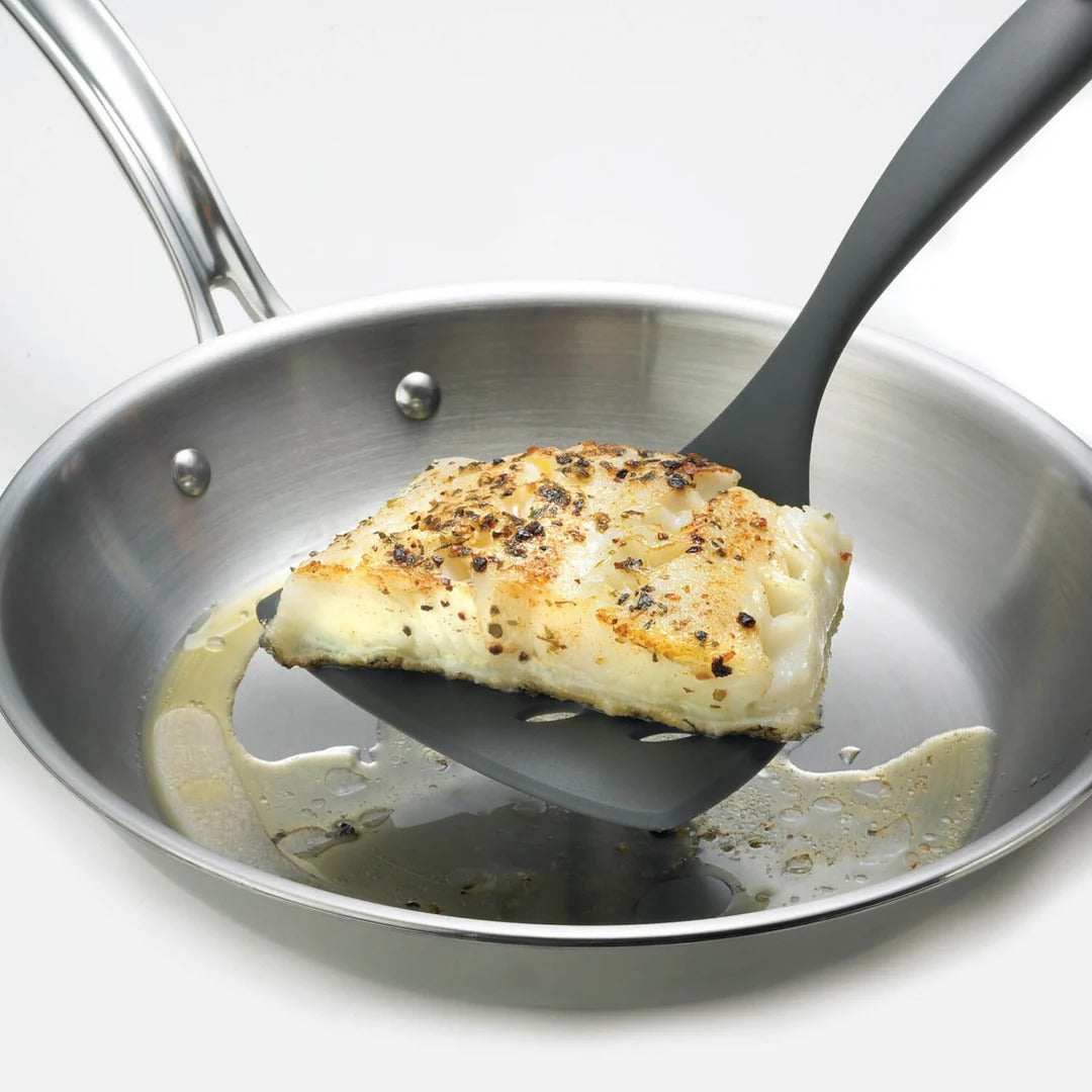 Wide turner lifting chicken in skillet; dark perforated head, red handle