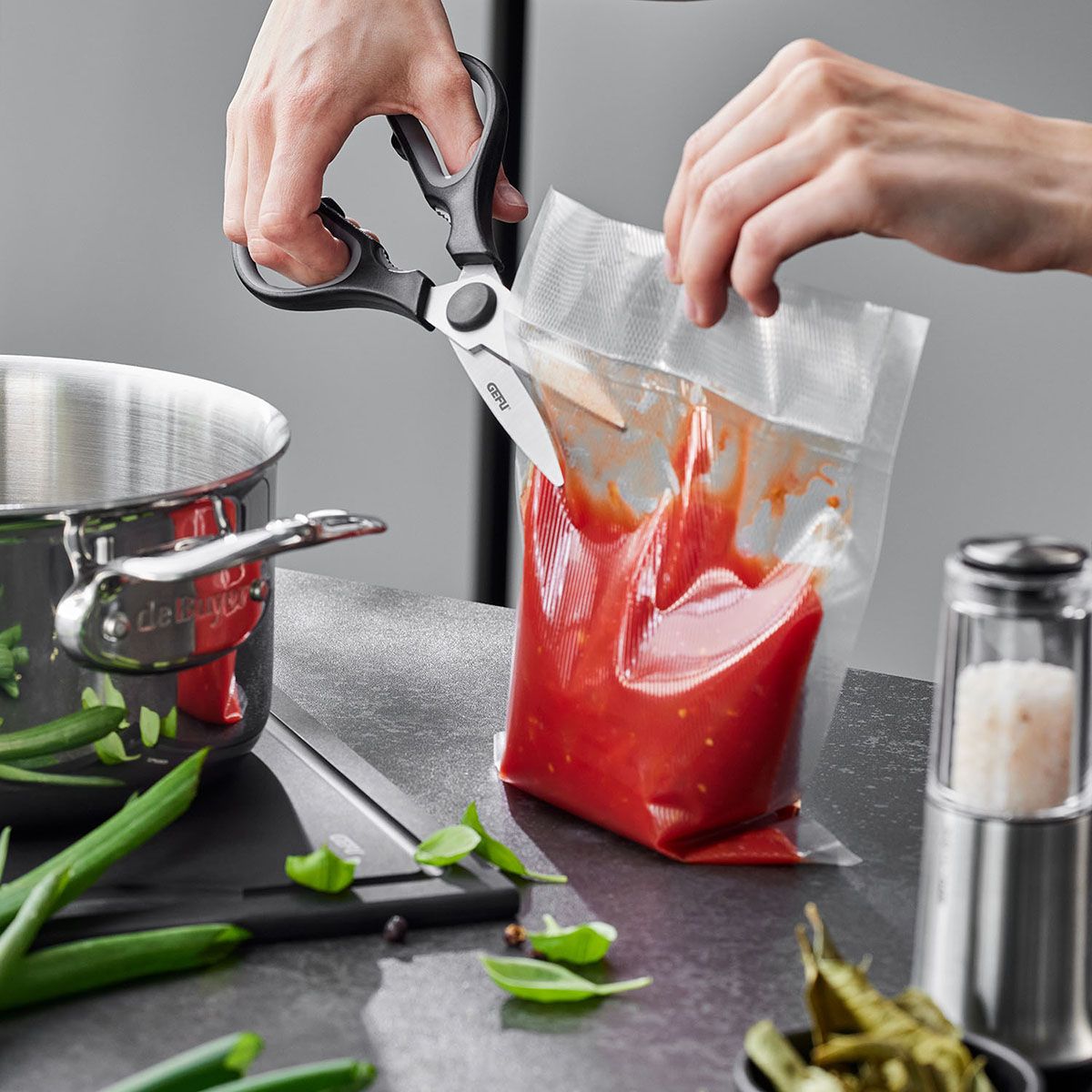 Handheld general-purpose scissors with dark handles cutting a plastic bag
