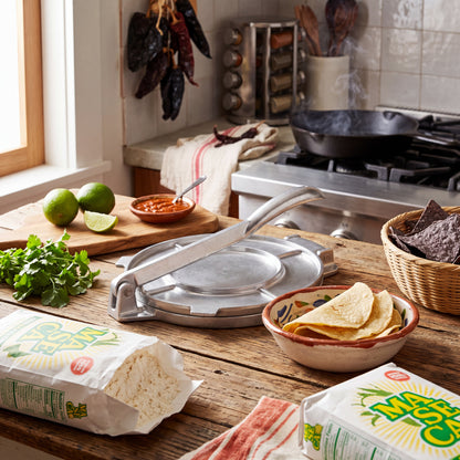 Stainless steel tortilla press with hinged handle on a wooden countertop.