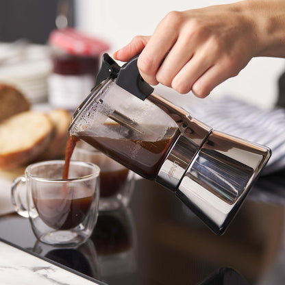 Person pouring coffee from a French press into a glass mug on a kitchen counter.