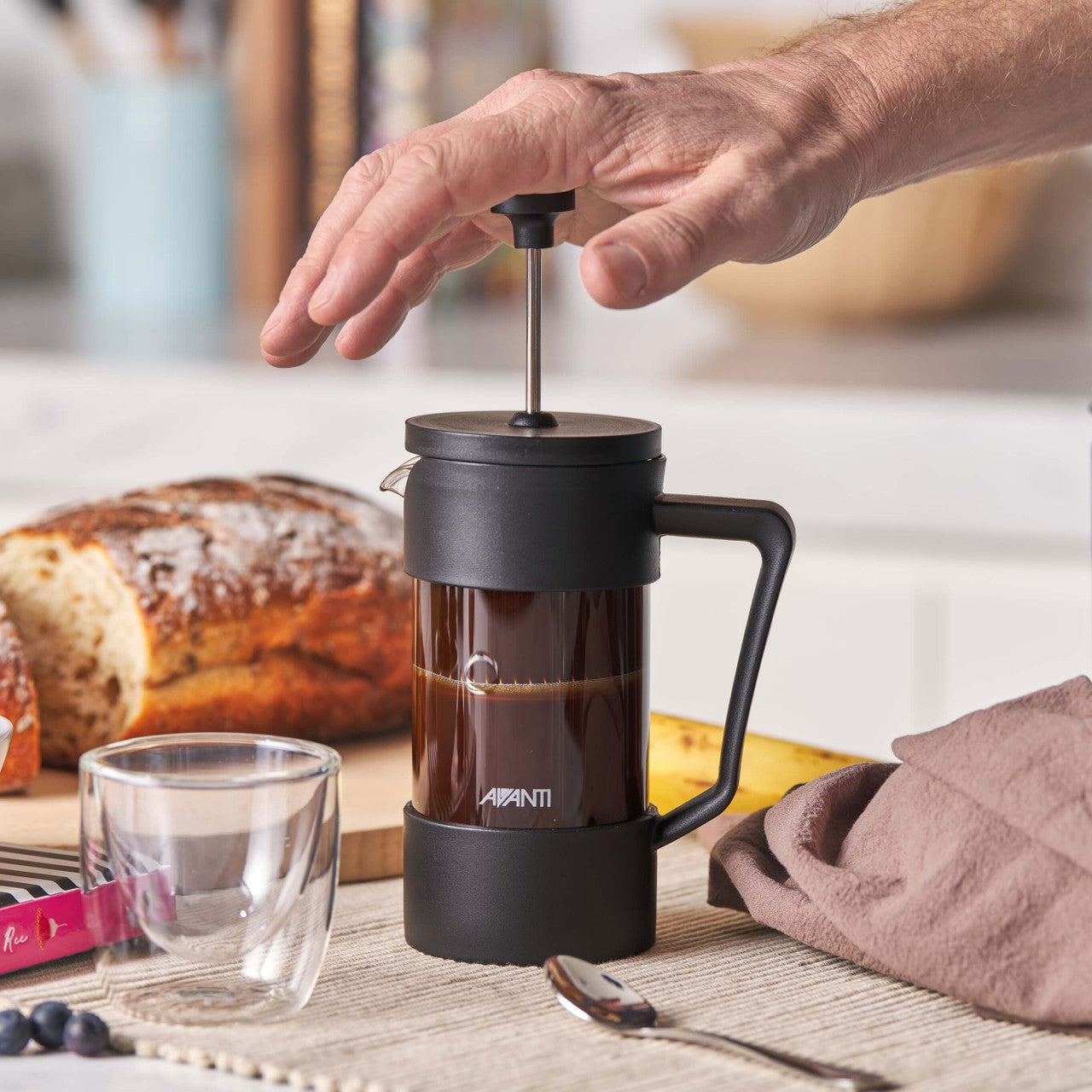 Person using a French press coffee maker with a blurred kitchen background