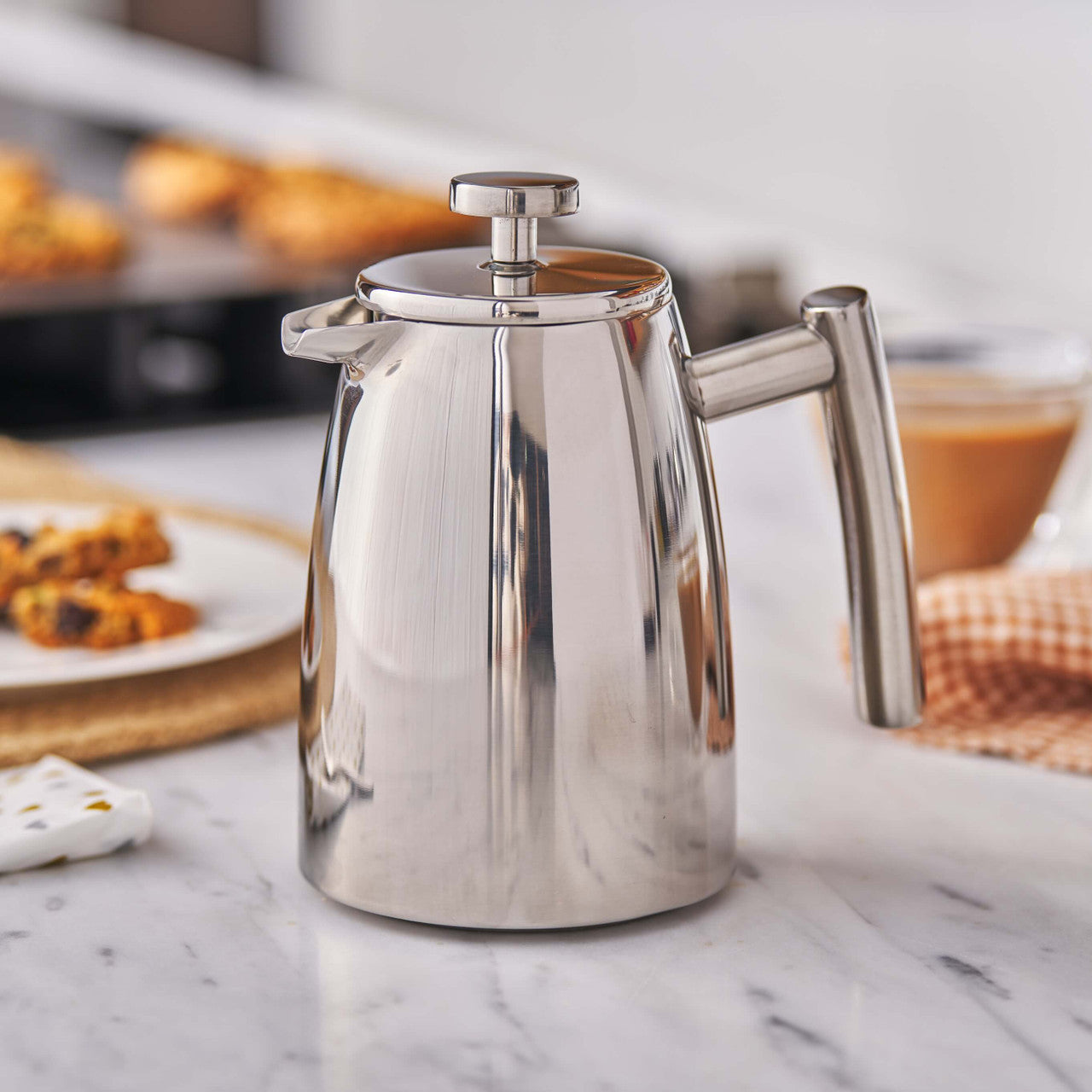 Stainless steel coffee pot on a marble countertop with pastries in the background