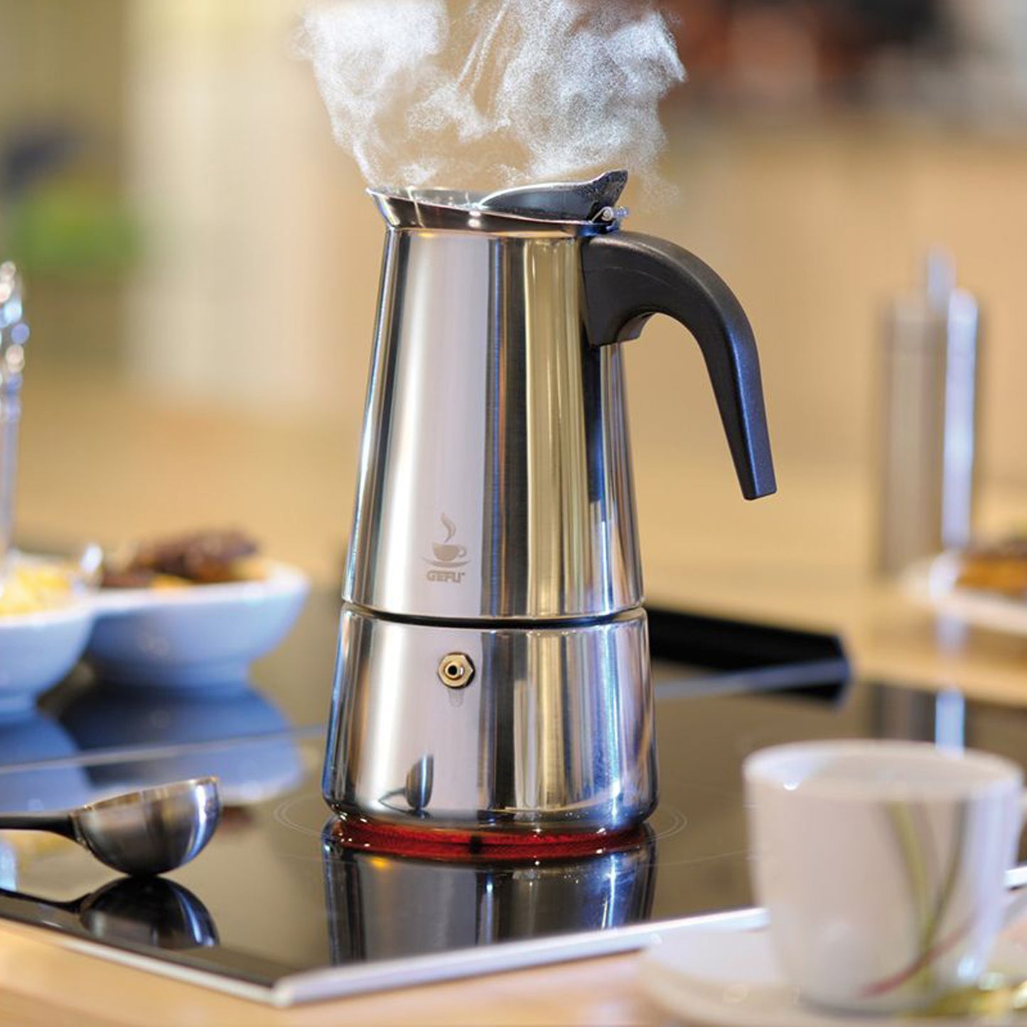 Stainless espresso maker with black handle, steam rising from spout