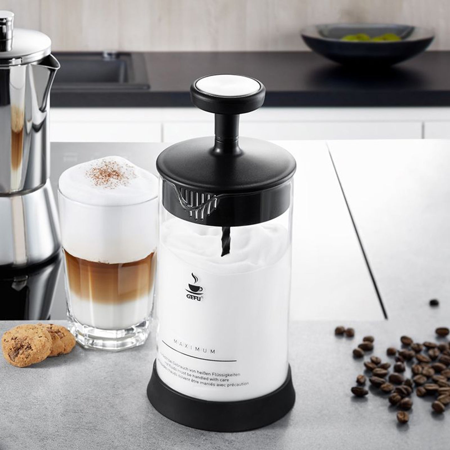 Milk frother on countertop with frothy milk in glass beside it