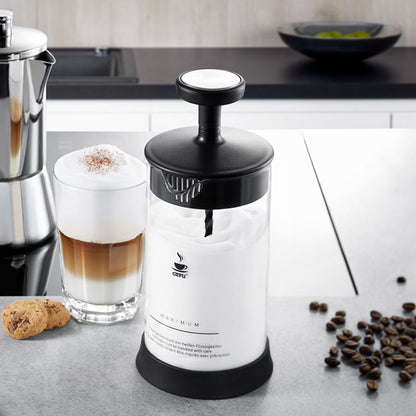 Milk frother on countertop with frothy milk in glass beside it