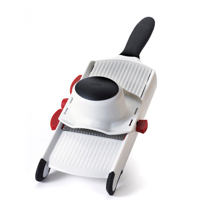 Handheld mandoline slicer, white body with black handle and red control knobs.