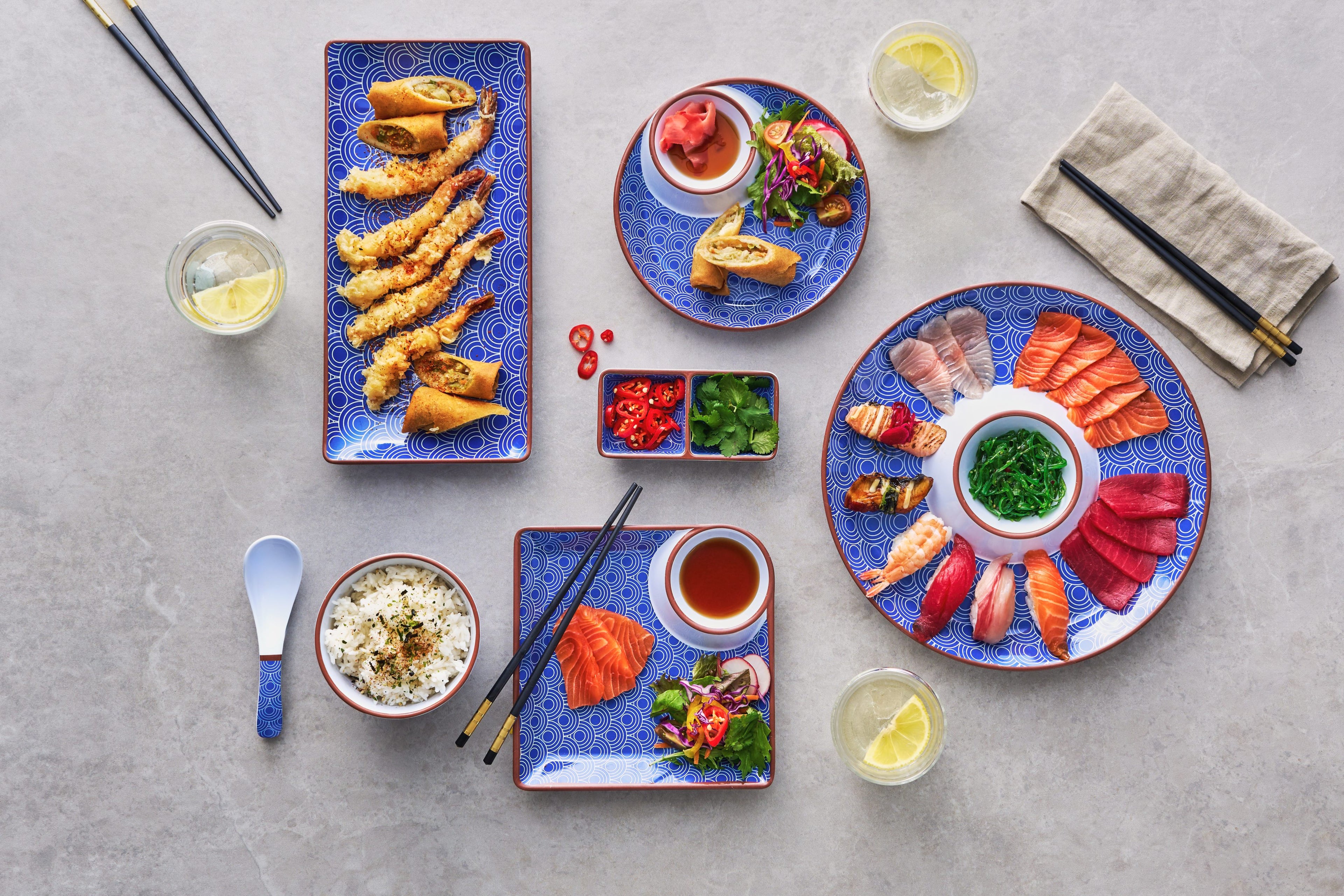 Assorted Japanese cuisine on blue plates with garnishes on a gray surface