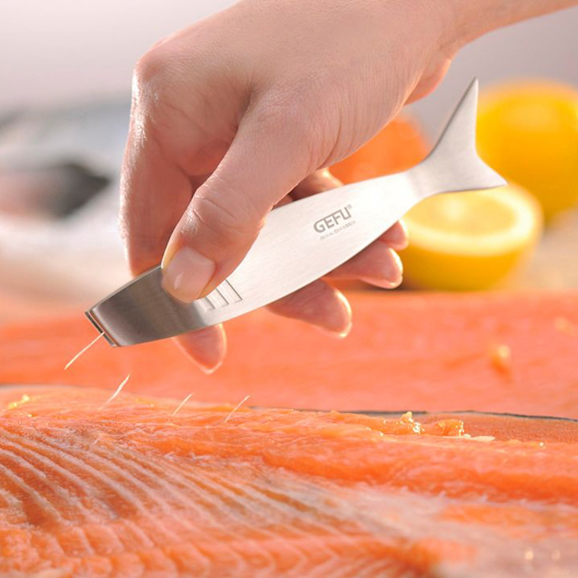 Fish bone tweezers pulling a thin bone from salmon fillet, held in hand.