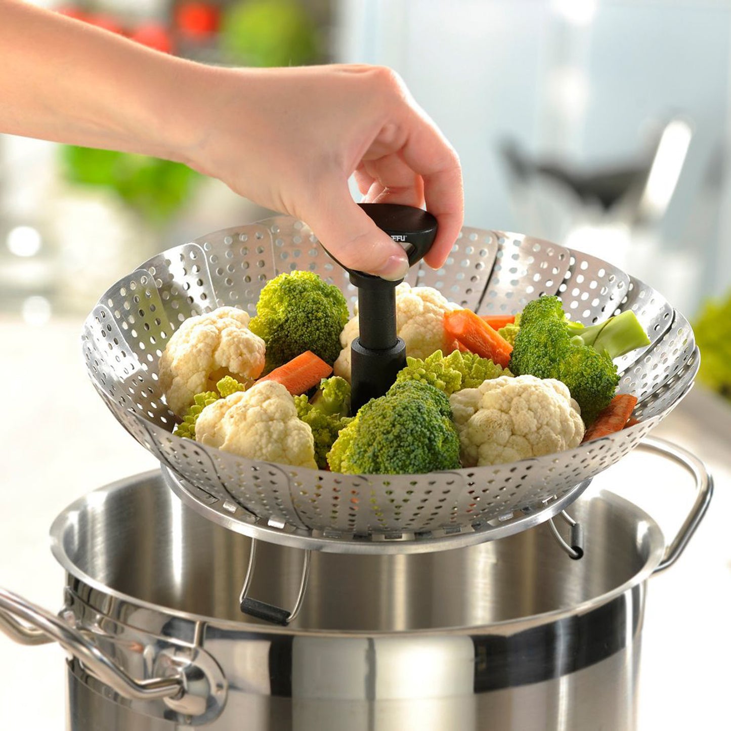 Hand lifting perforated metal steam insert with black handle over pot