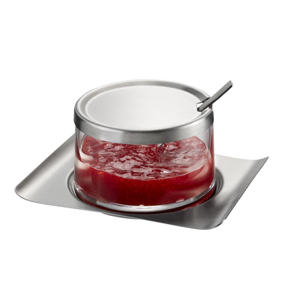 Glass jam jar with metal lid and spoon, filled with red jam on tray
