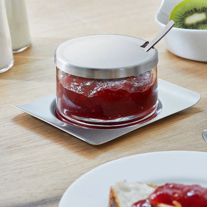 Glass jam jar with metal lid and spoon, filled with red jam on metal tray