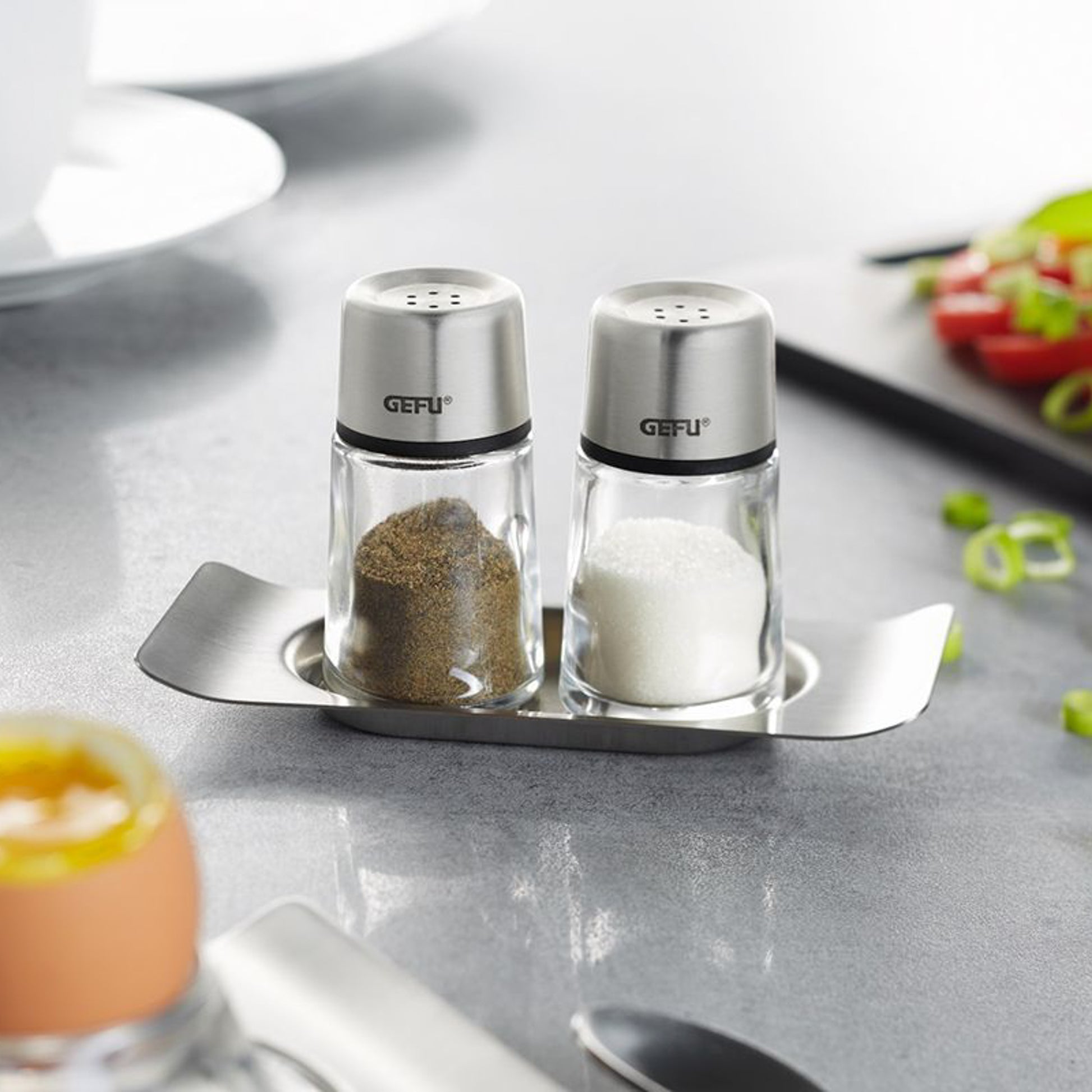 Stainless steel salt and pepper shakers on metal tray with contents visible