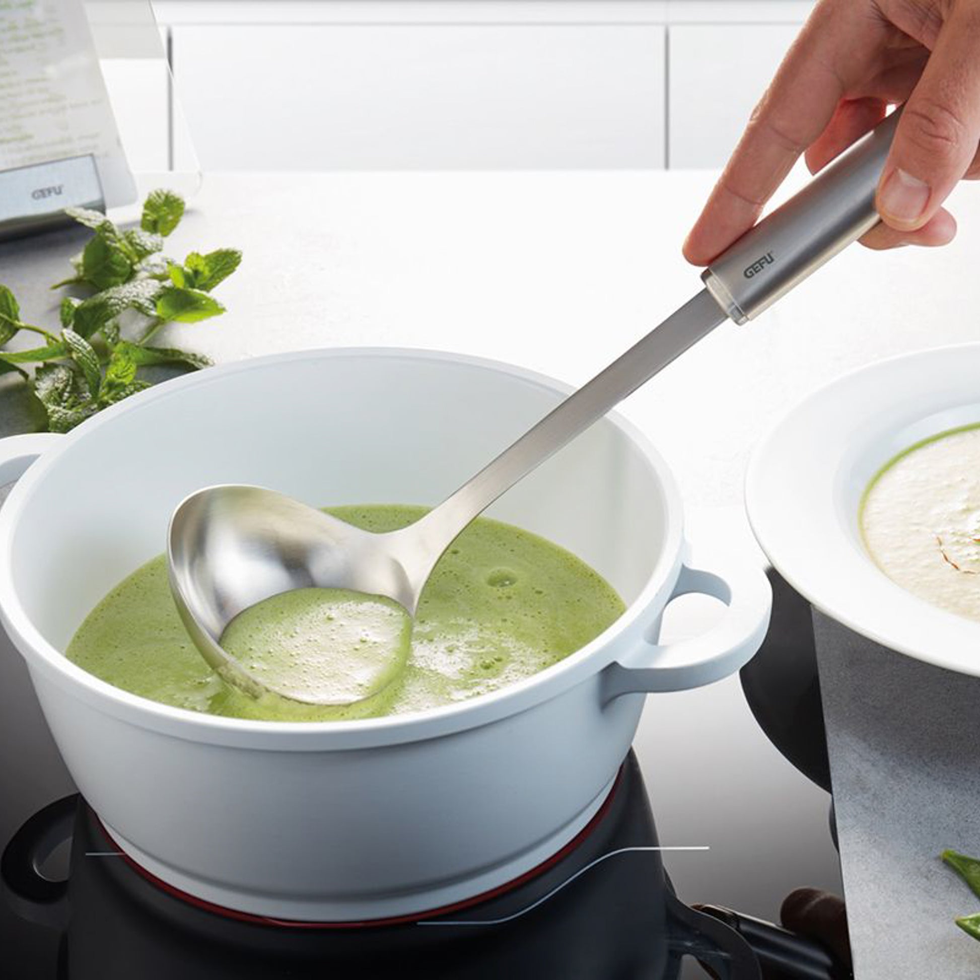 Stainless steel ladle with black handle stirring green soup in a pot