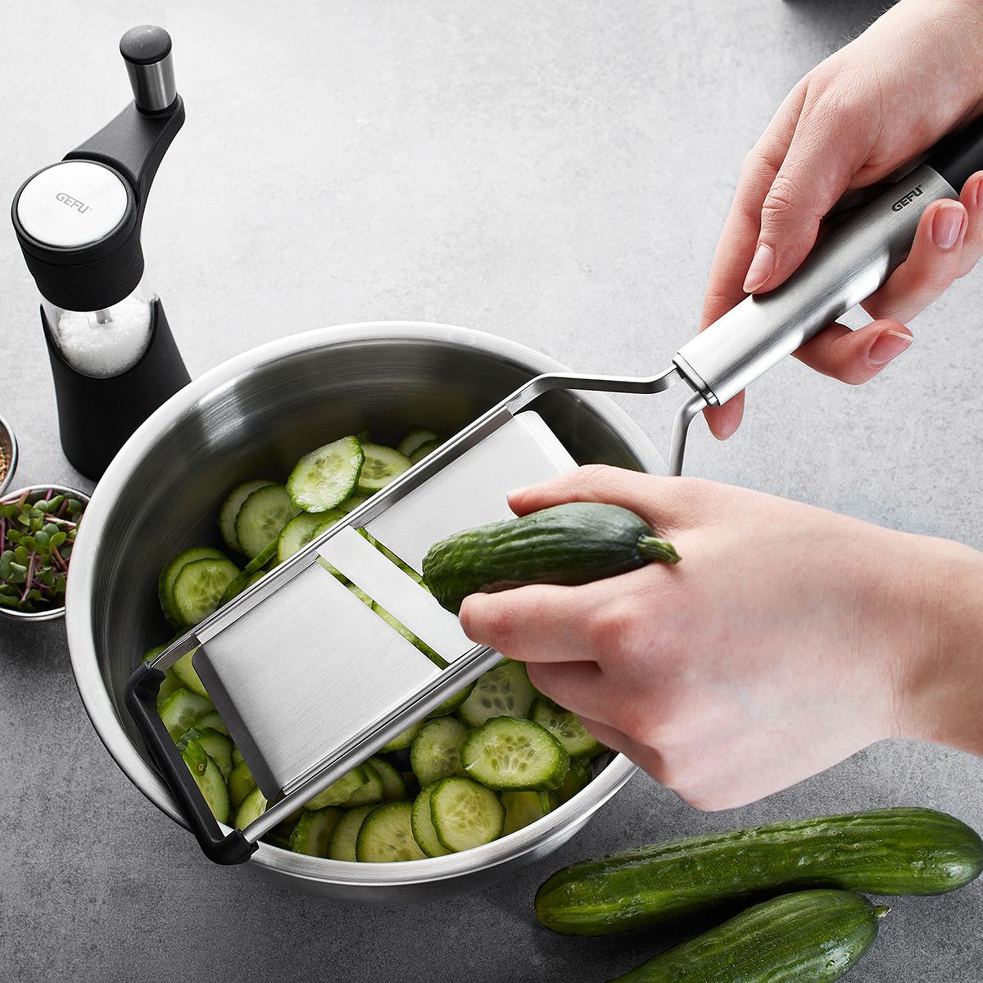 Vegetable slicer in use: hands slide blade to slice cucumber over a pot