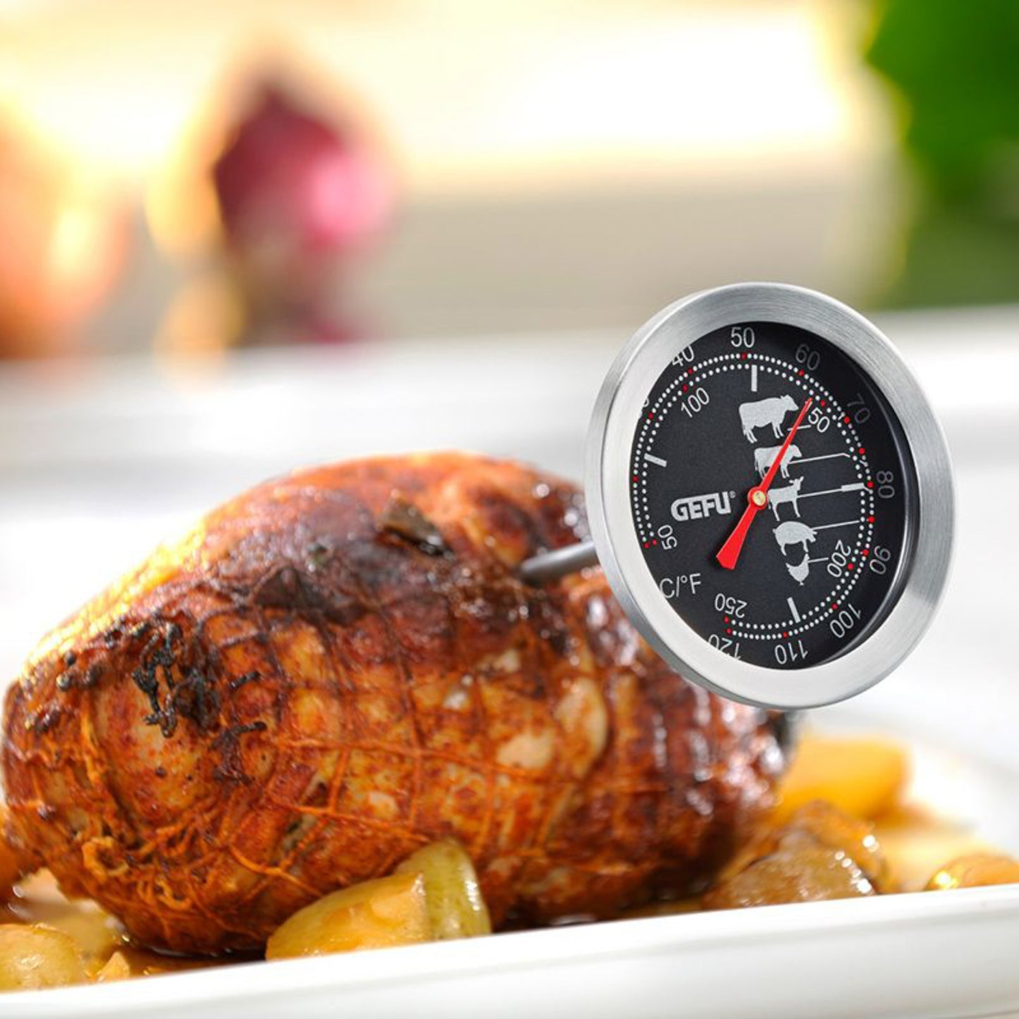 Roast thermometer placed on serving dish beside roasted meat, dial with °C/°F