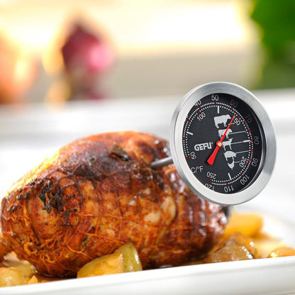 Roast thermometer placed on serving dish beside roasted meat, dial with °C/°F