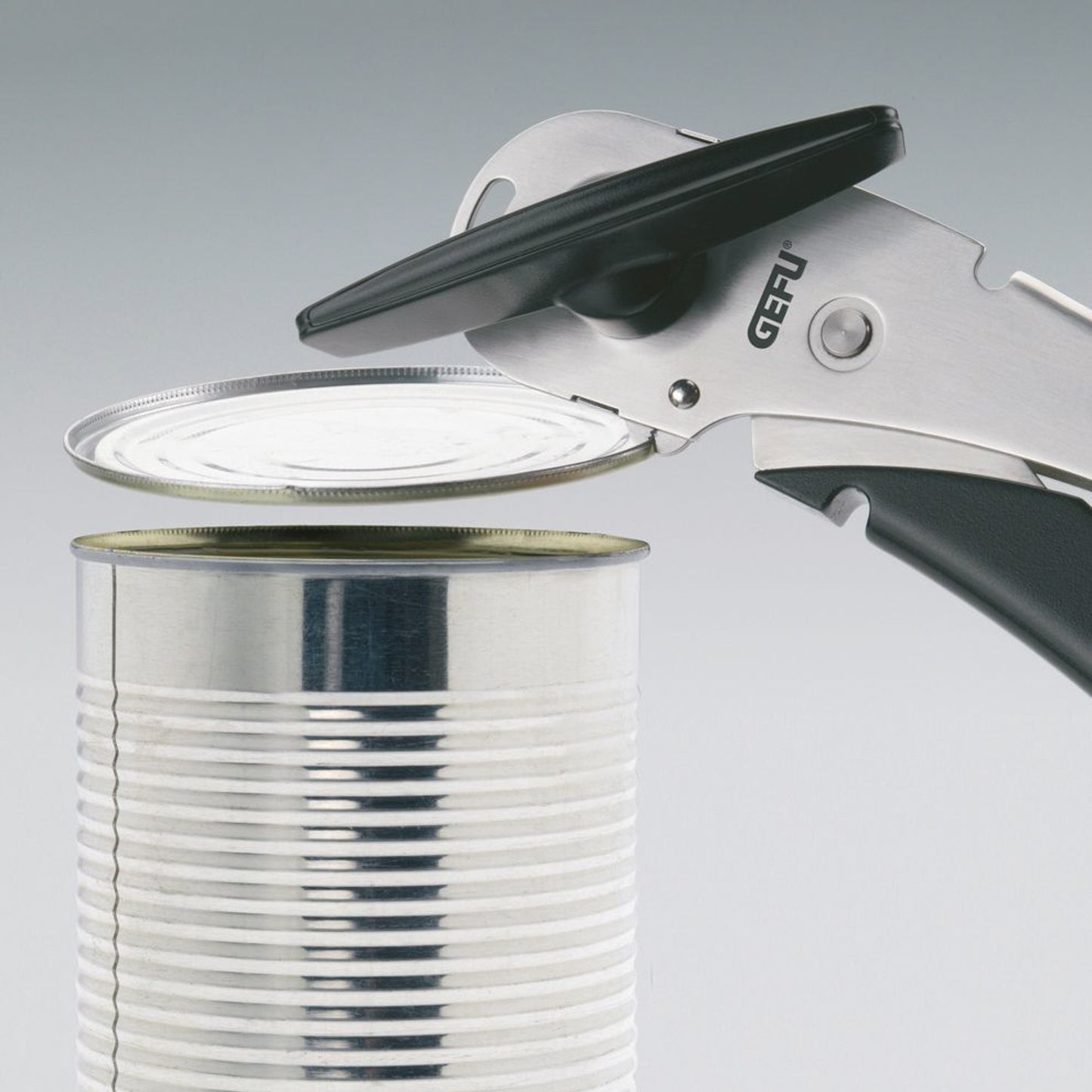 Manual can opener cutting end near metal can lid with black handle