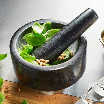 Black stone mortar and pestle with leafy greens and garlic