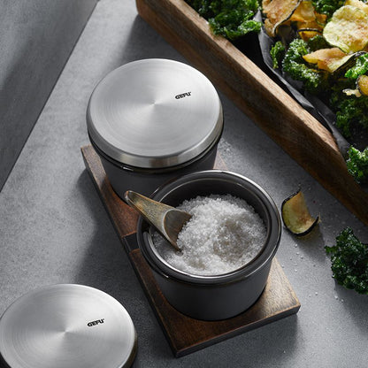 Black salt and spice pot with stainless lid, wooden tray, and spoon with white salt