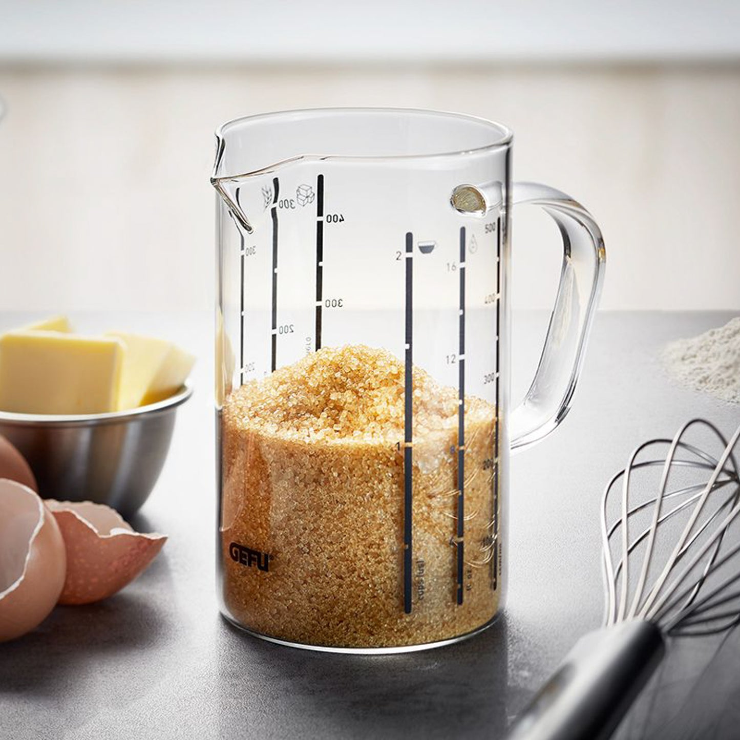 Clear measuring jug with spout and handle, showing ml and L markings; filled with golden grains
