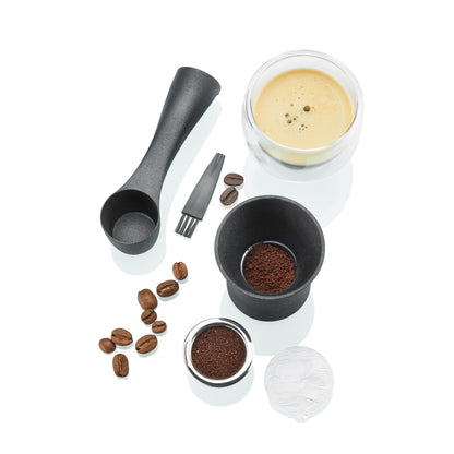 Coffee capsule brewing set with black scoop, cup, capsules, and coffee grounds