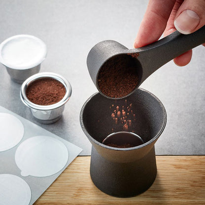 Hand using black coffee scoop to fill a capsule cup with coffee grounds