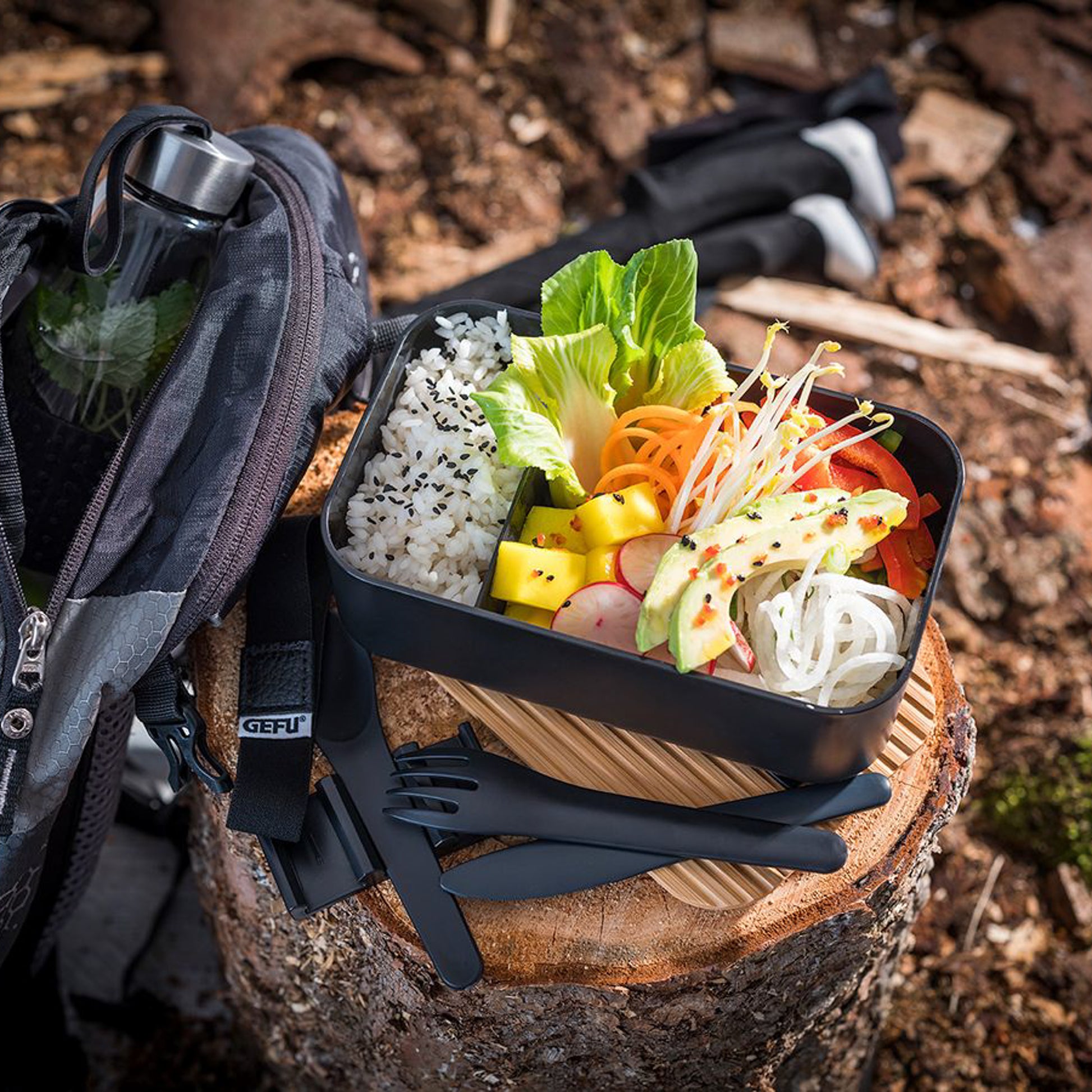 Black bento-style lunch box with bamboo base, open for meal prep with utensils