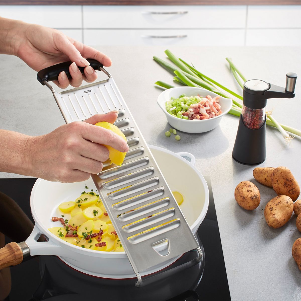 Stainless steel potato slicer with black handle, cutting a potato into thin slices