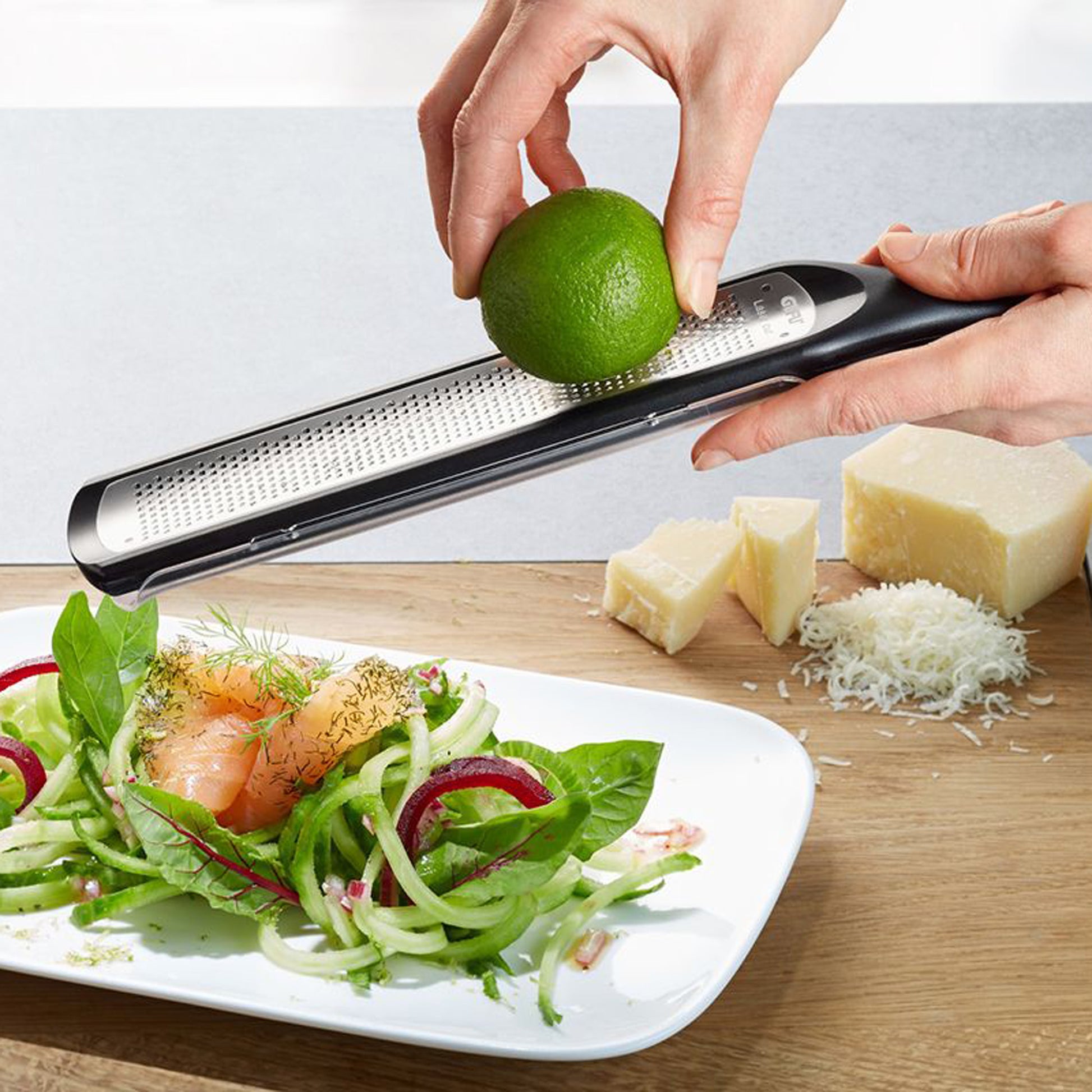 Fine grater in use: hands hold a green lime over the perforated surface