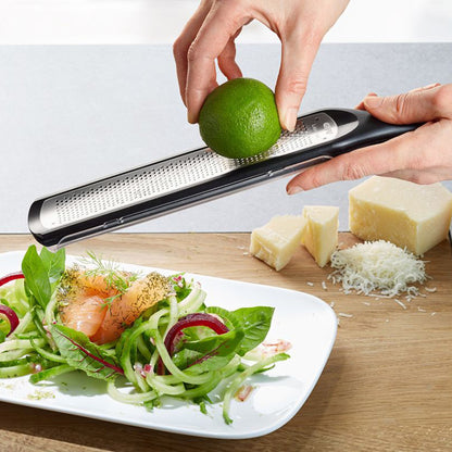 Fine grater in use: hands hold a green lime over the perforated surface