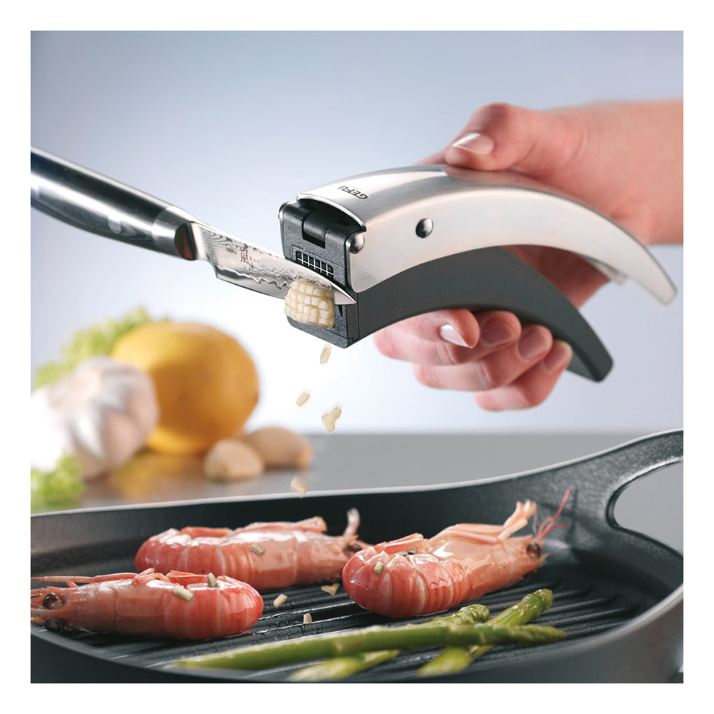Garlic cutter with silver handle and black base, held over garlic cloves