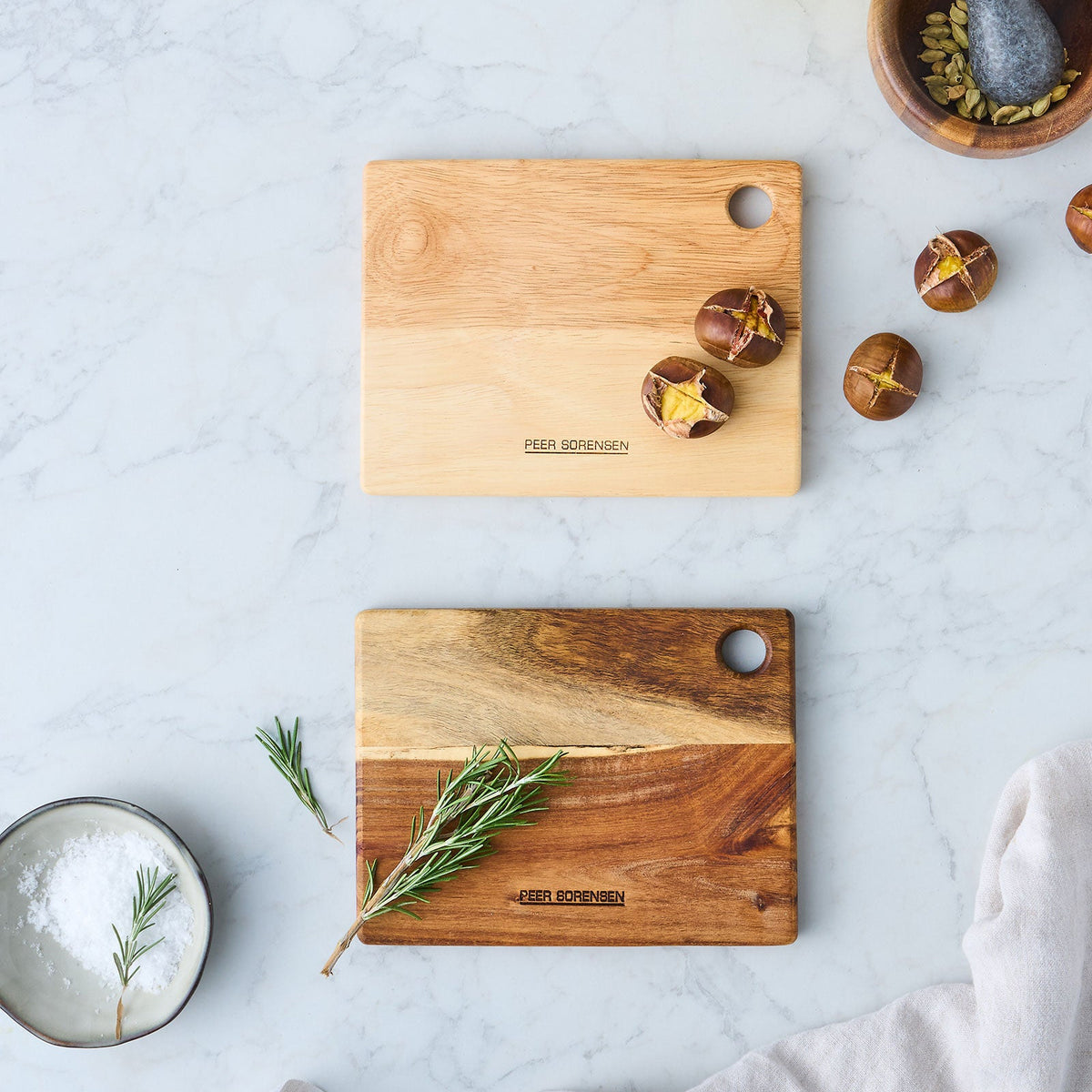 Two wooden utility cutting boards with hanging holes and scattered herbs