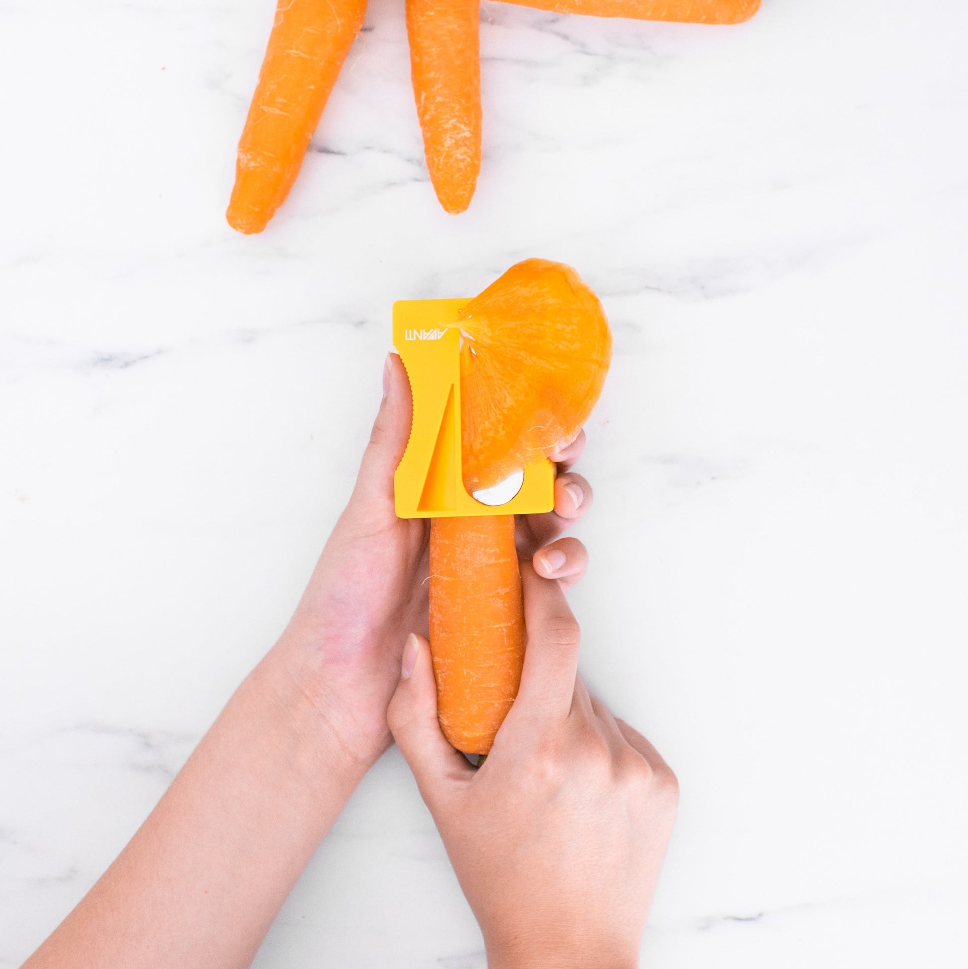 Person using a carrot peeler on carrots on a white marble surface