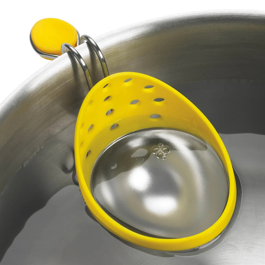Perforated yellow egg poacher cup with metal rim on stainless steel pan