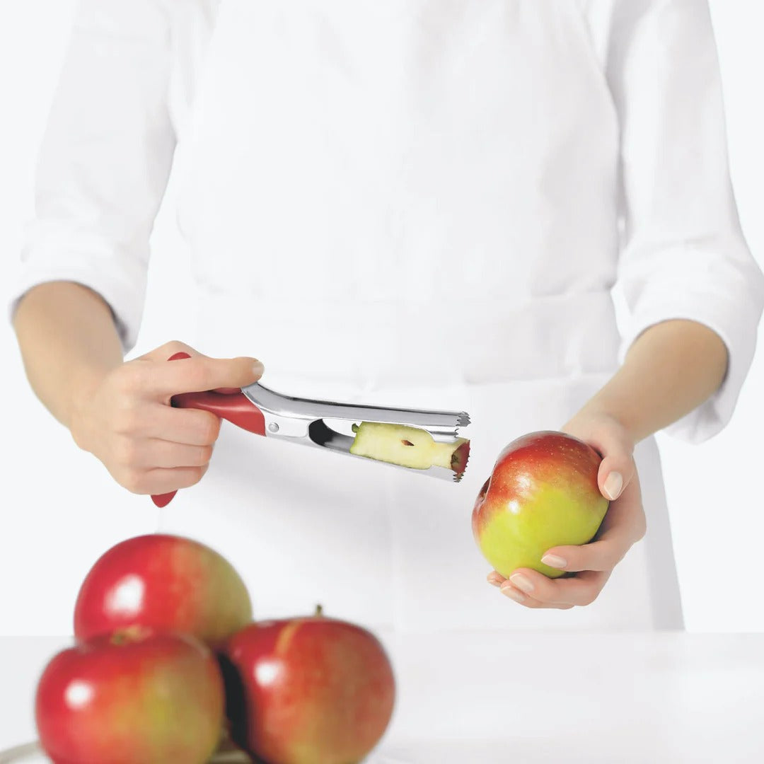 Hands using red-handled apple corer to remove a core from a red apple