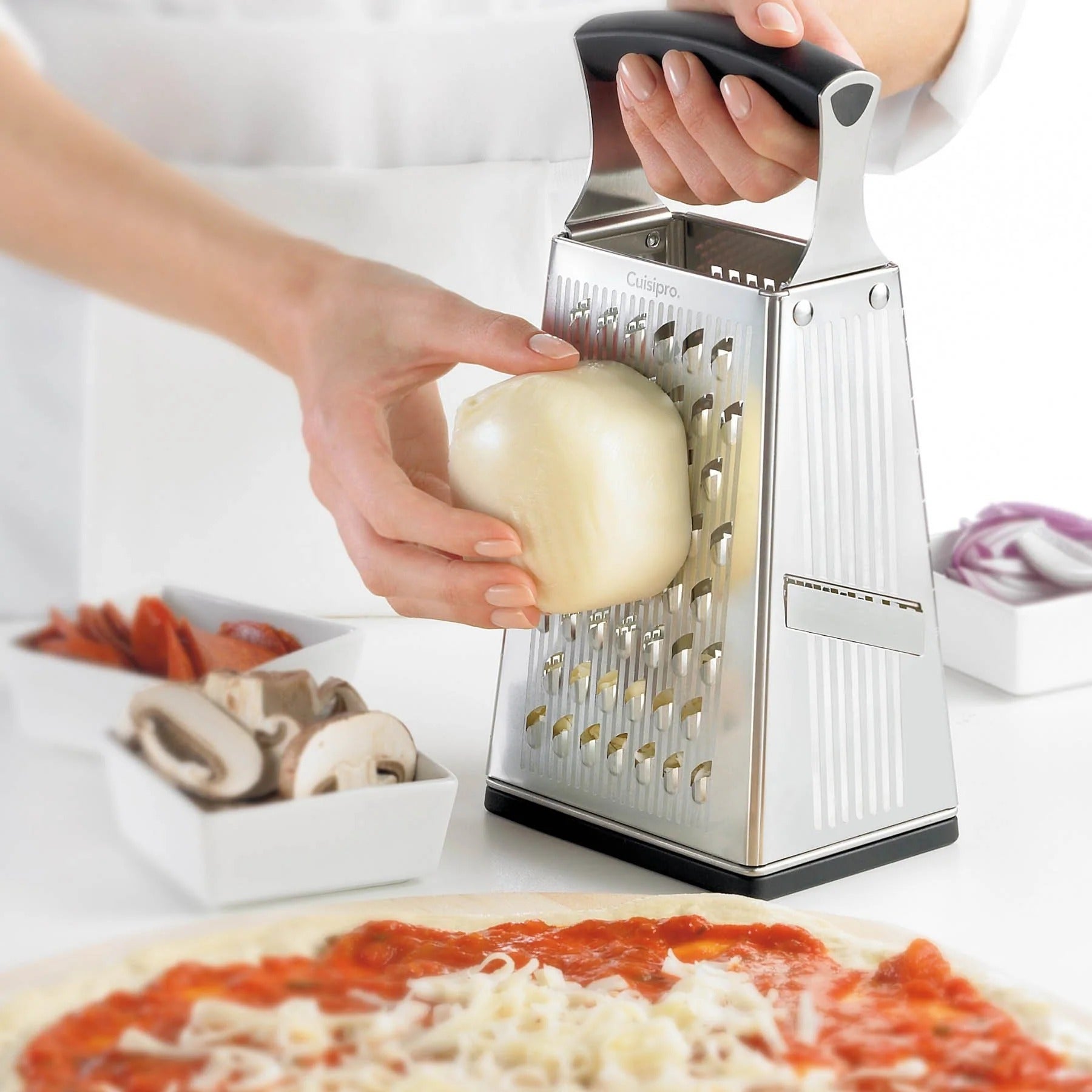 Box grater grating a peeled onion over chopped vegetables