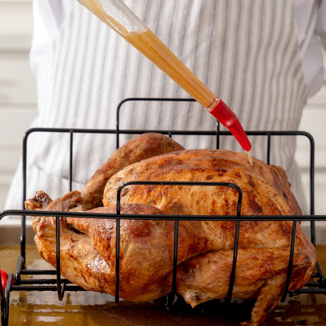 Turkey baster with wooden handle and red brush tip over roasted chicken
