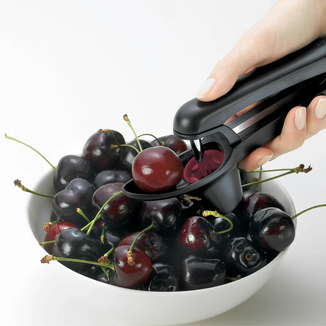 Handheld pitter tool pressing through cherries into the red collection cup
