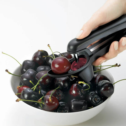Handheld pitter tool pressing through cherries into the red collection cup