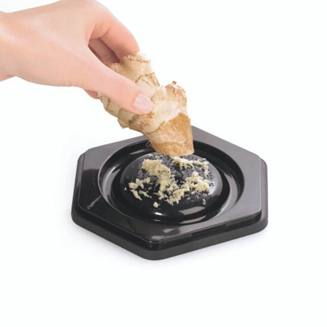 Box grater in use: hand grating pale food over a black base tray